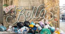 Basura sin recoger en la calle ante una pared con una pintada que dice "La Vita e Bella"